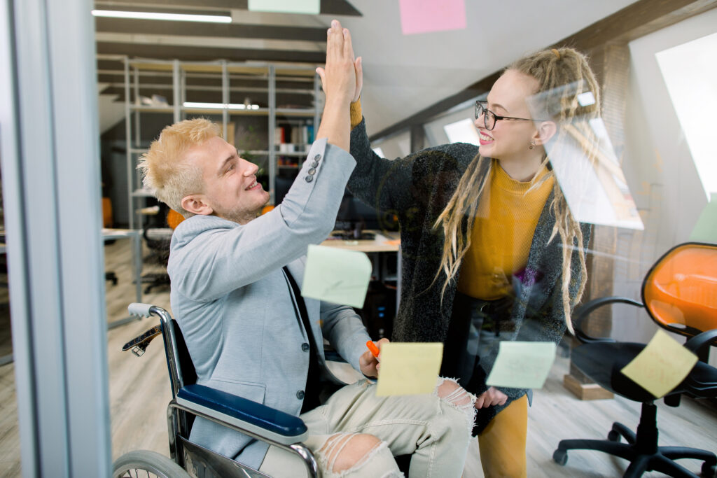 Smiling man in a wheelchair high-fiving a coworker in the office