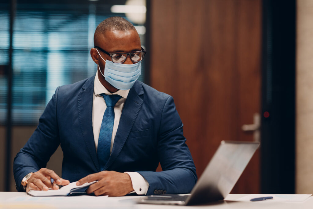 Smiling businessman in a face mask seated at a meeting table in an office