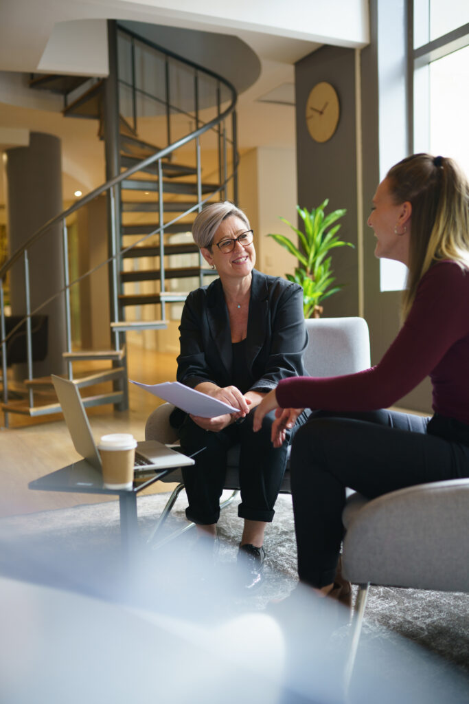 Smiling businesswoman with a laptop and coffee reviewing a document with a coworker