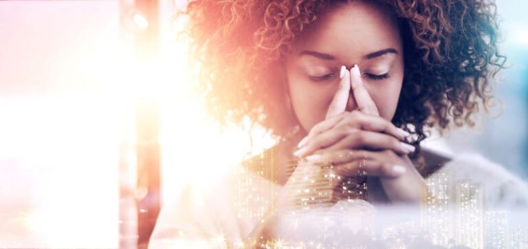Woman with curly hair sitting with eyes closed and fingers pressed to her face, appearing stressed or deep in thought, with a soft double exposure effect of a cityscape and bright light.