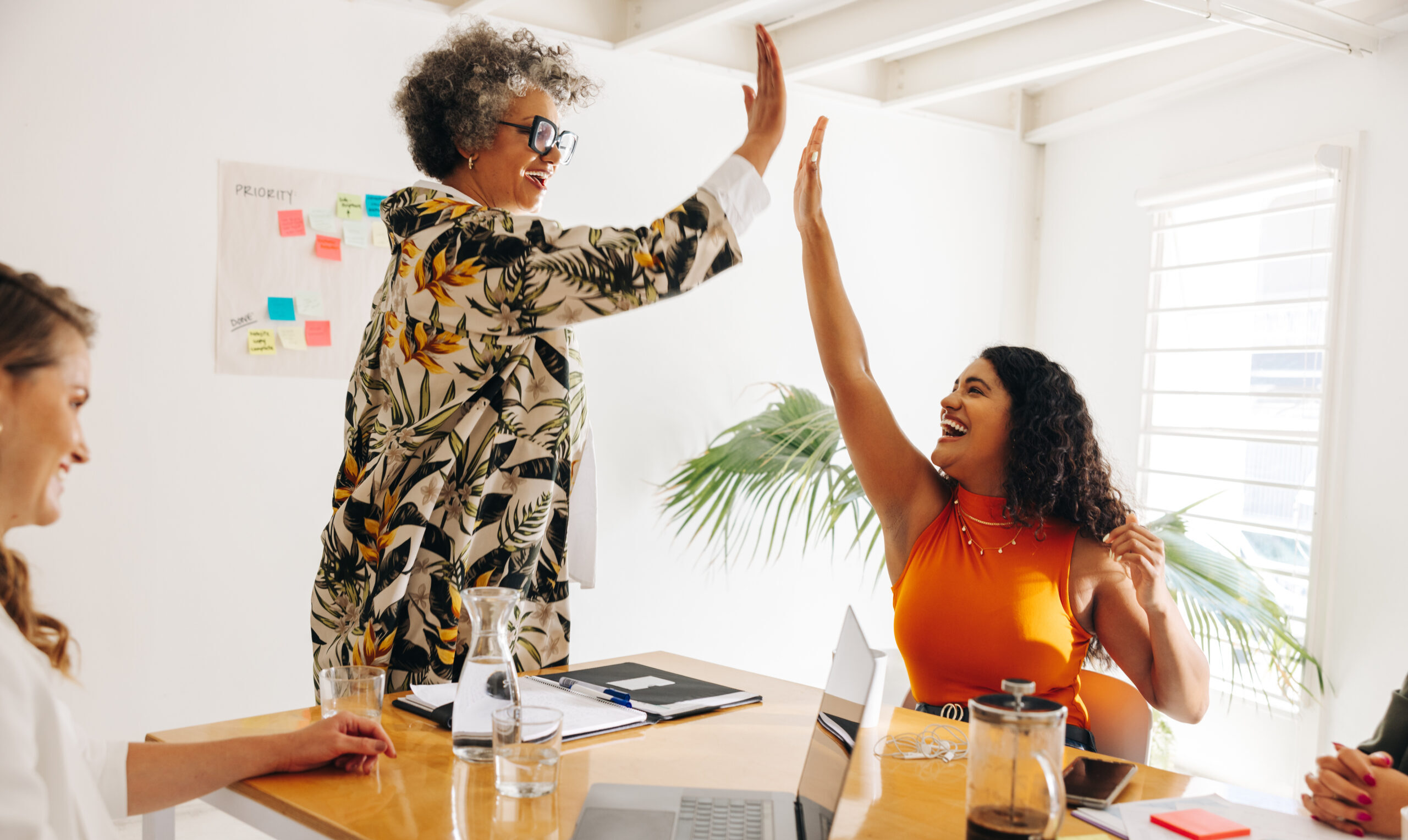 Successful businesswomen high fiving each other during a meeting in a boardroom. Happy businesswomen celebrating their achievement in an office.