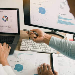 hands pointing working together on a computer pointing at the screen with pie charts and graphs on the screen