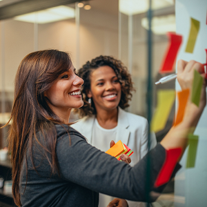 Two woman standing at a white board, one writing, on it