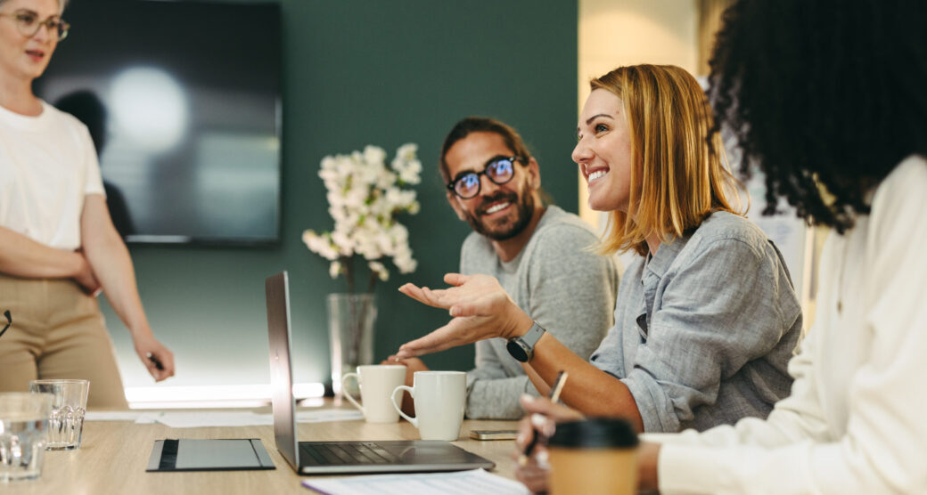 Business woman talking to her colleagues during a meeting in a boardroom. Group of happy business people working together in a creative office.