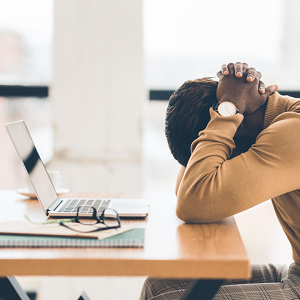 frustrated person sitting at a computer with head down and hands interlaced behind their head