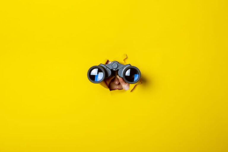 Female hand holds black binoculars on a yellow background. Journey, find and search concept.