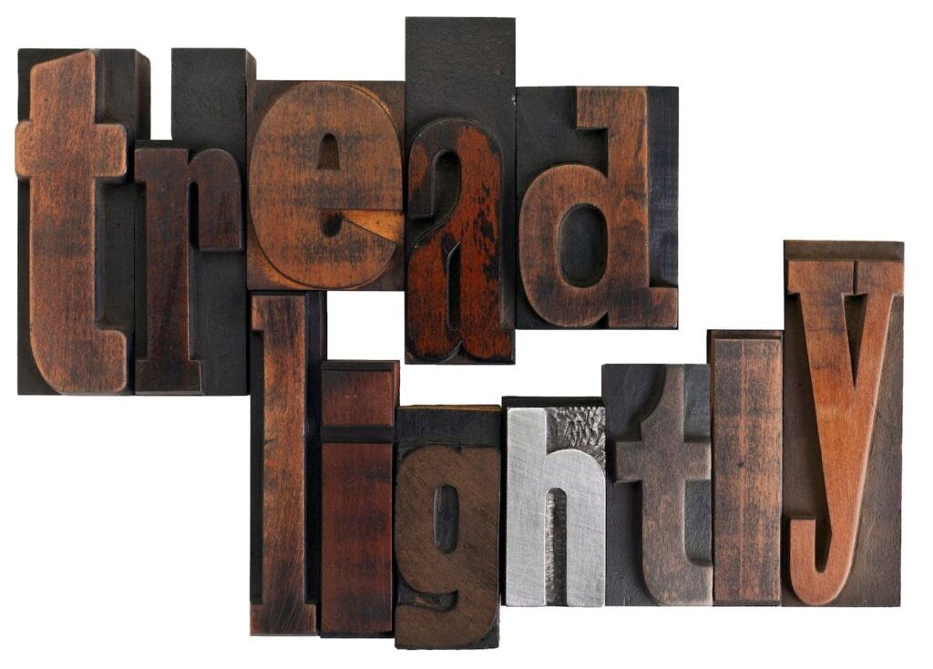 The phrase "tread lightly" is spelled out using vintage wooden and metal letterpress blocks in varying shades of brown, black, and silver, arranged in a tight, overlapping layout against a white background.