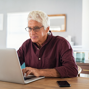 older man with glasses sitting at table on a computer