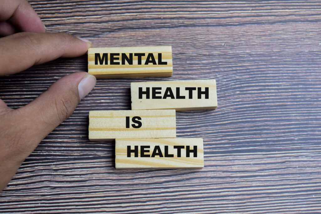 Hand arranging wooden blocks with the phrase “Mental health is health” on a wood background, symbolizing the importance of mental well-being.
