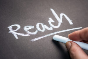 Hand writing the word REACH on chalkboard, social media concept