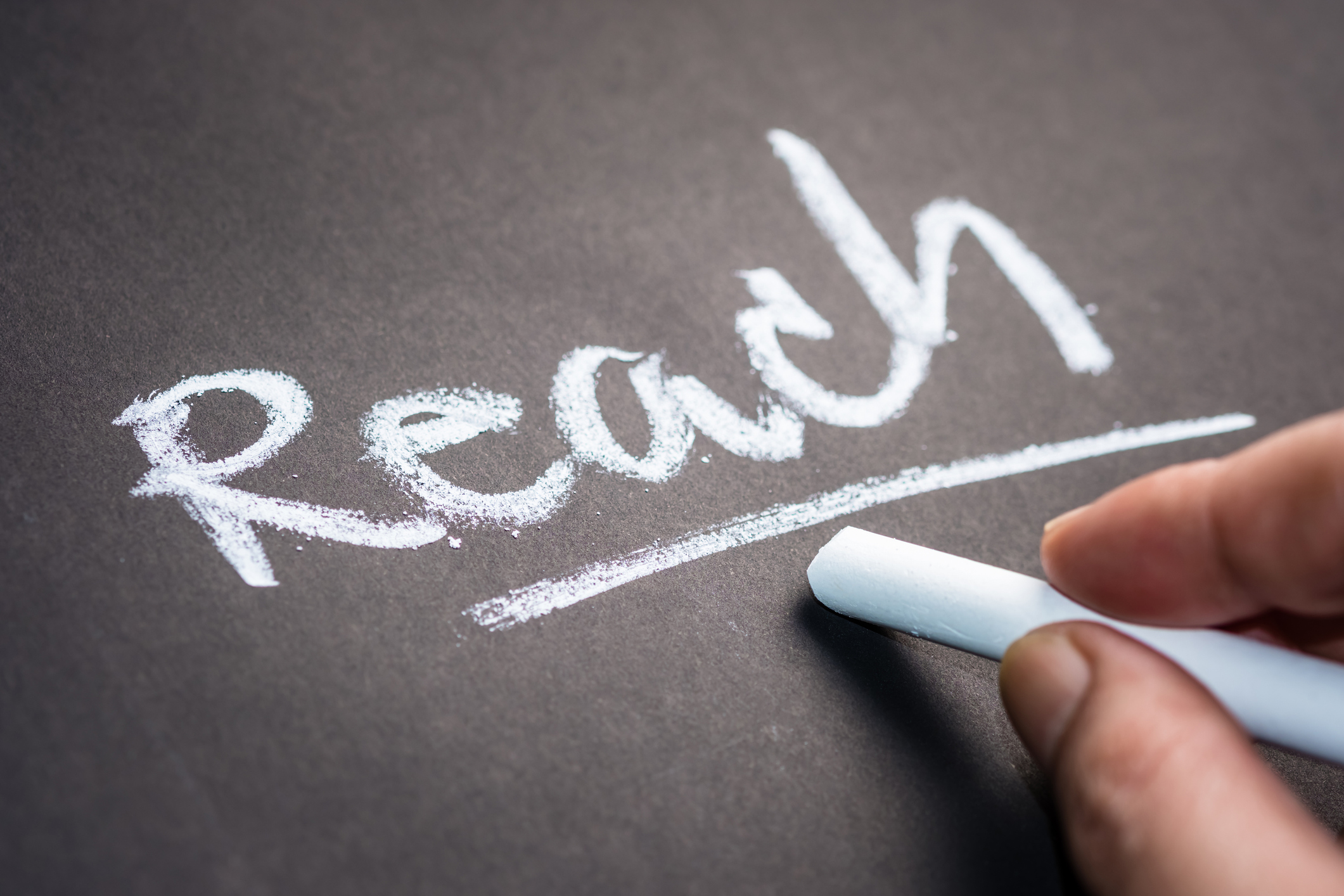 Hand writing the word REACH on chalkboard, social media concept